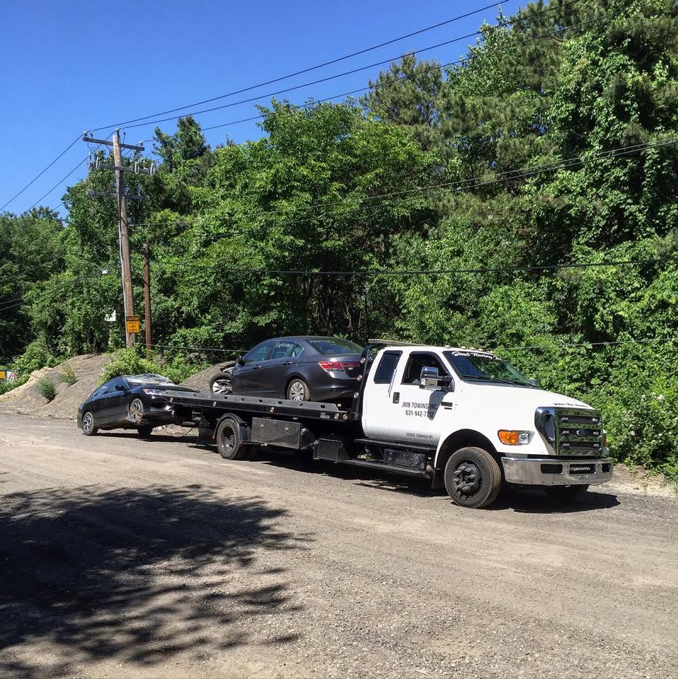 JMB Towing flatbed truck towing two vehicles on a gravel road