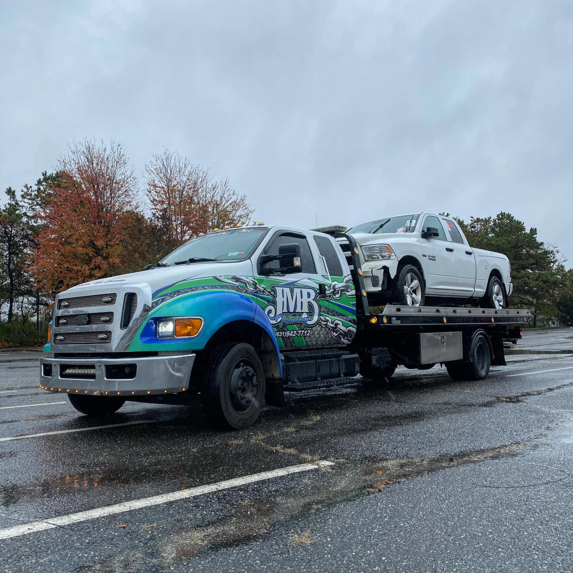 JMB Towing flatbed truck carrying a pickup truck on a rainy day