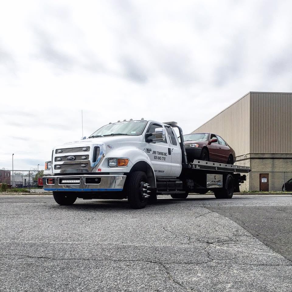 JMB Towing flatbed truck loaded with a sedan in a parking lot