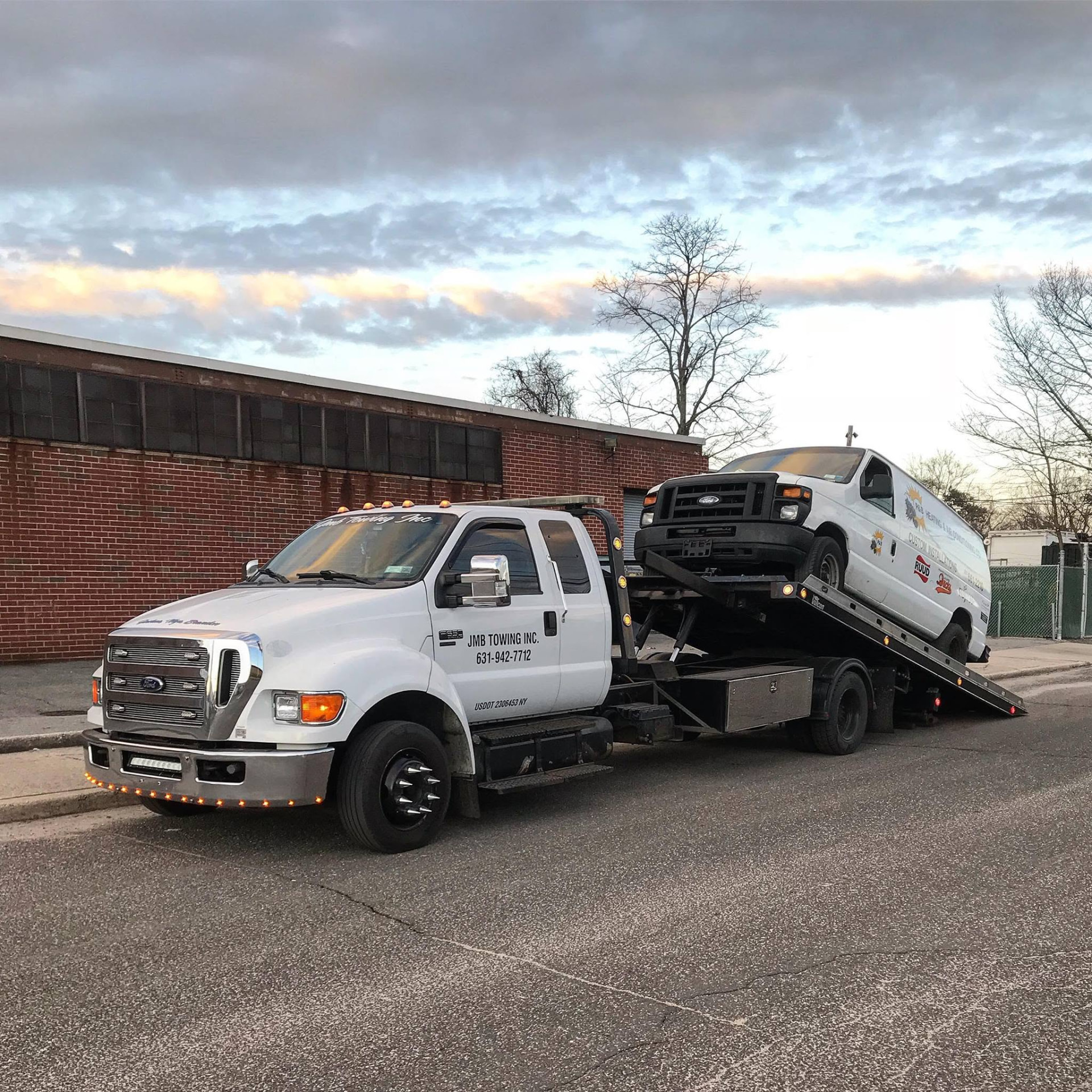 JMB Towing flatbed truck transporting a van at dusk